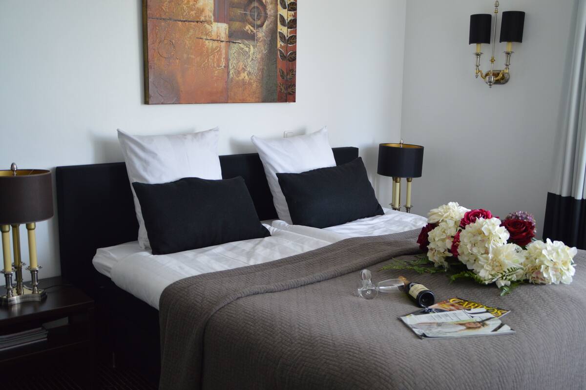 A hotel room with a neatly made bed, a bouquet of flowers, and a magazine on the bed.