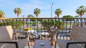 A balcony with wicker furniture, a table, and a view of palm trees and parked cars. - Wien Star Hotel (Alanya)