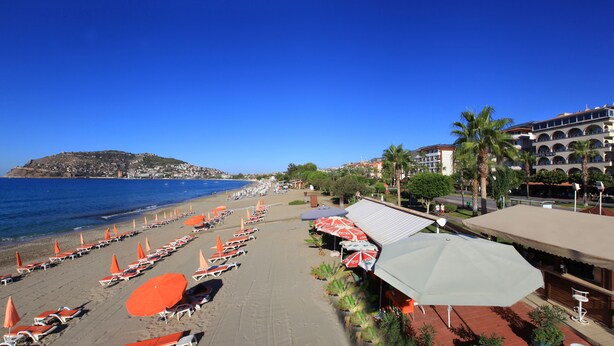 A beach with rows of sun loungers and umbrellas, a hotel named 'Hotel Wien' in the background, and a clear blue sky. - Wien Star Hotel (Alanya)