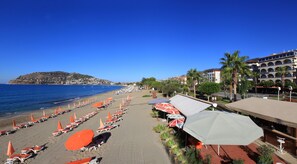 A beach with rows of sun loungers and umbrellas, a hotel named 'Hotel Wien' in the background, and a clear blue sky. - Wien Star Hotel (Alanya)