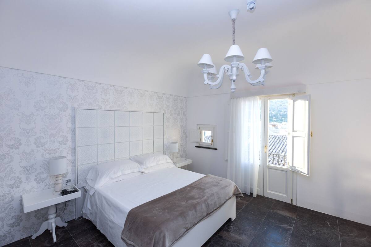 A bedroom with a bed, bedside table, lamp, and a chandelier.
