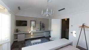 A modern bathroom with a large mirror, a chandelier, a sink, and a bench. - Palazzo Conti Camere & Suite (Scicli)