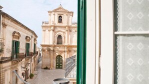 A view of a historic building with a bell tower, a cobblestone street, and a green door. - Palazzo Conti Camere & Suite (Scicli)