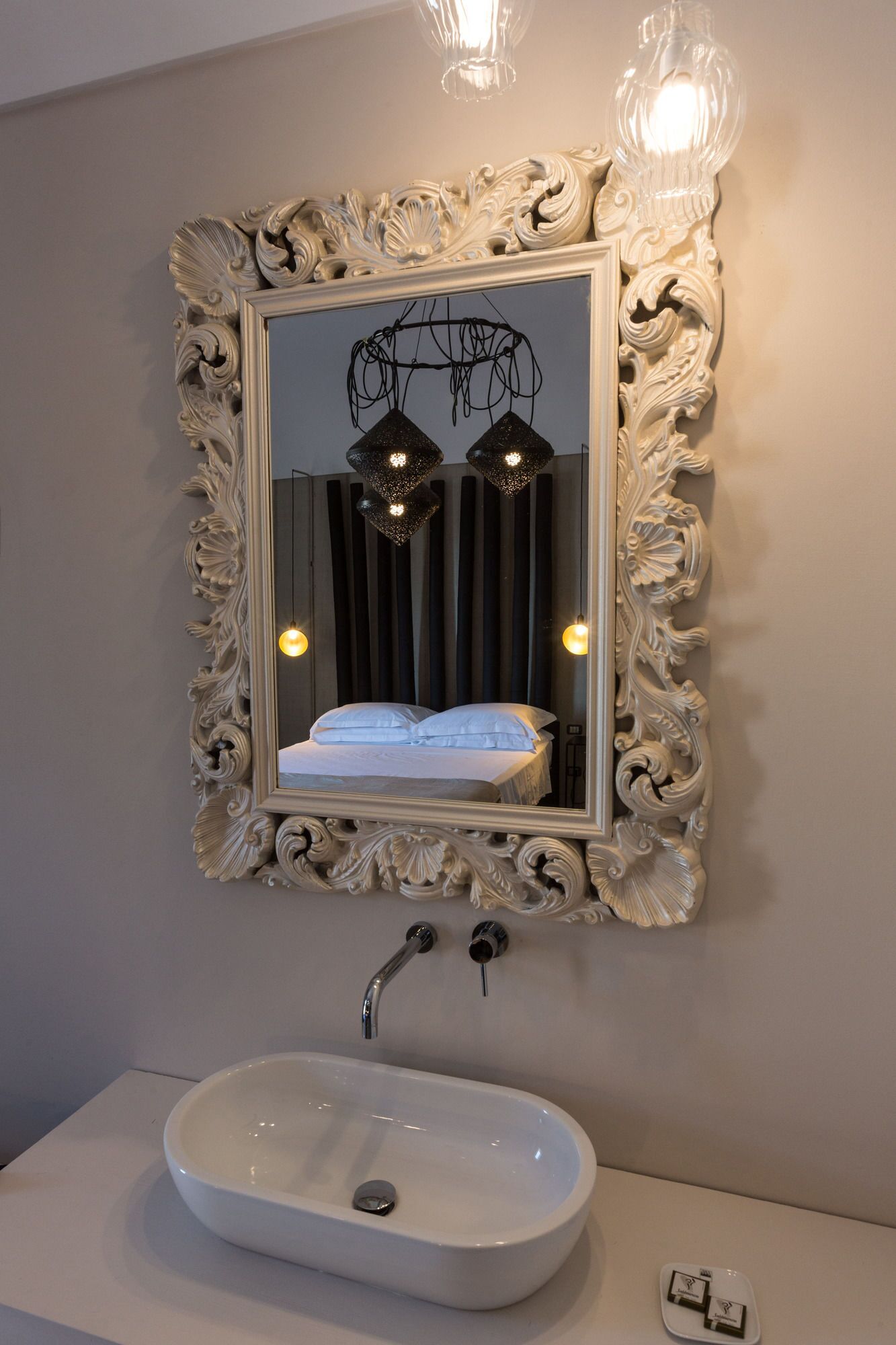 A bathroom with a large ornate mirror, a white sink, and two pendant lights above the mirror.