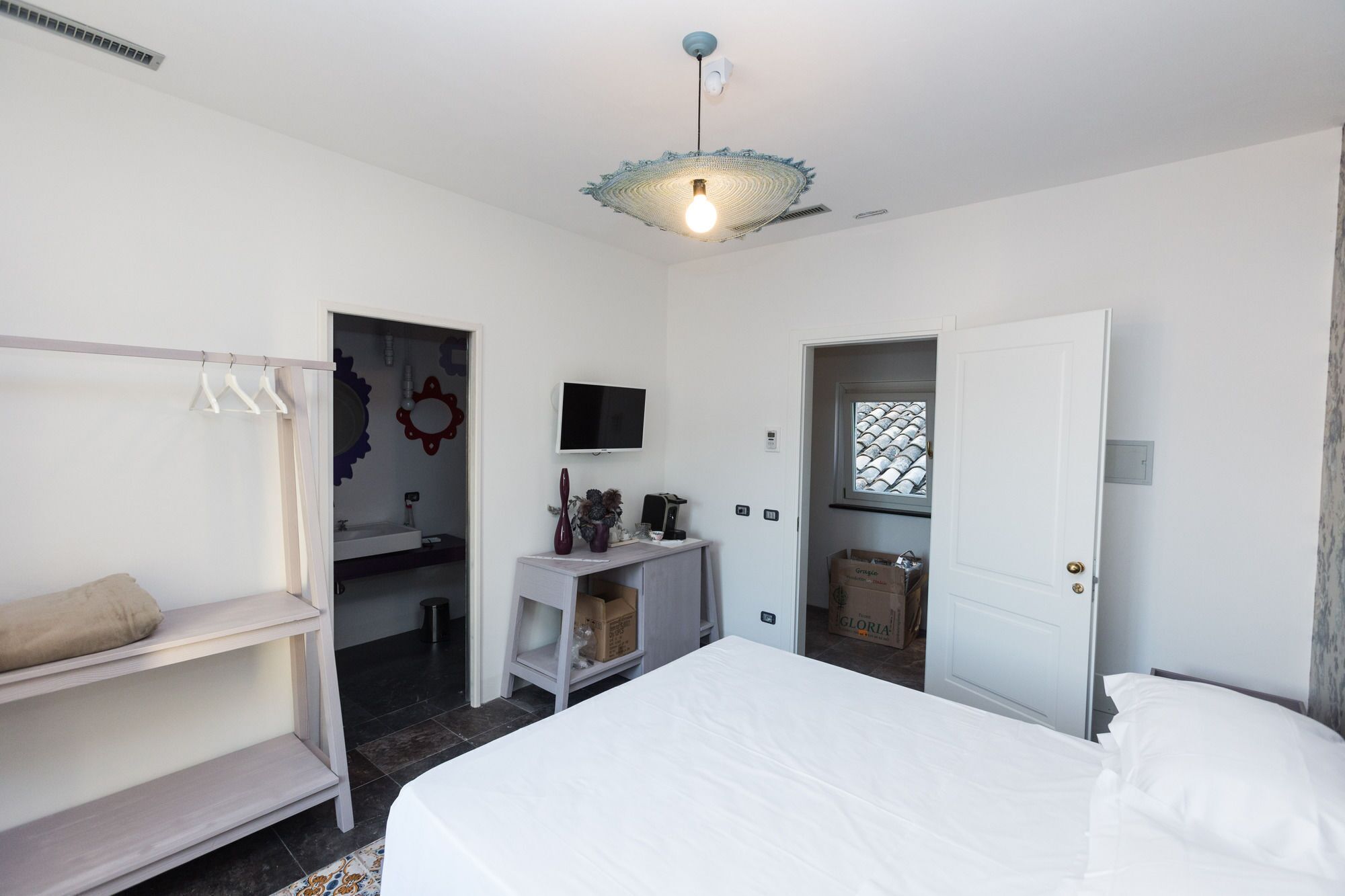 Una camera da letto con un letto, un armadio, una scrivania con sedia, una televisione e una porta che dà su un'altra stanza.