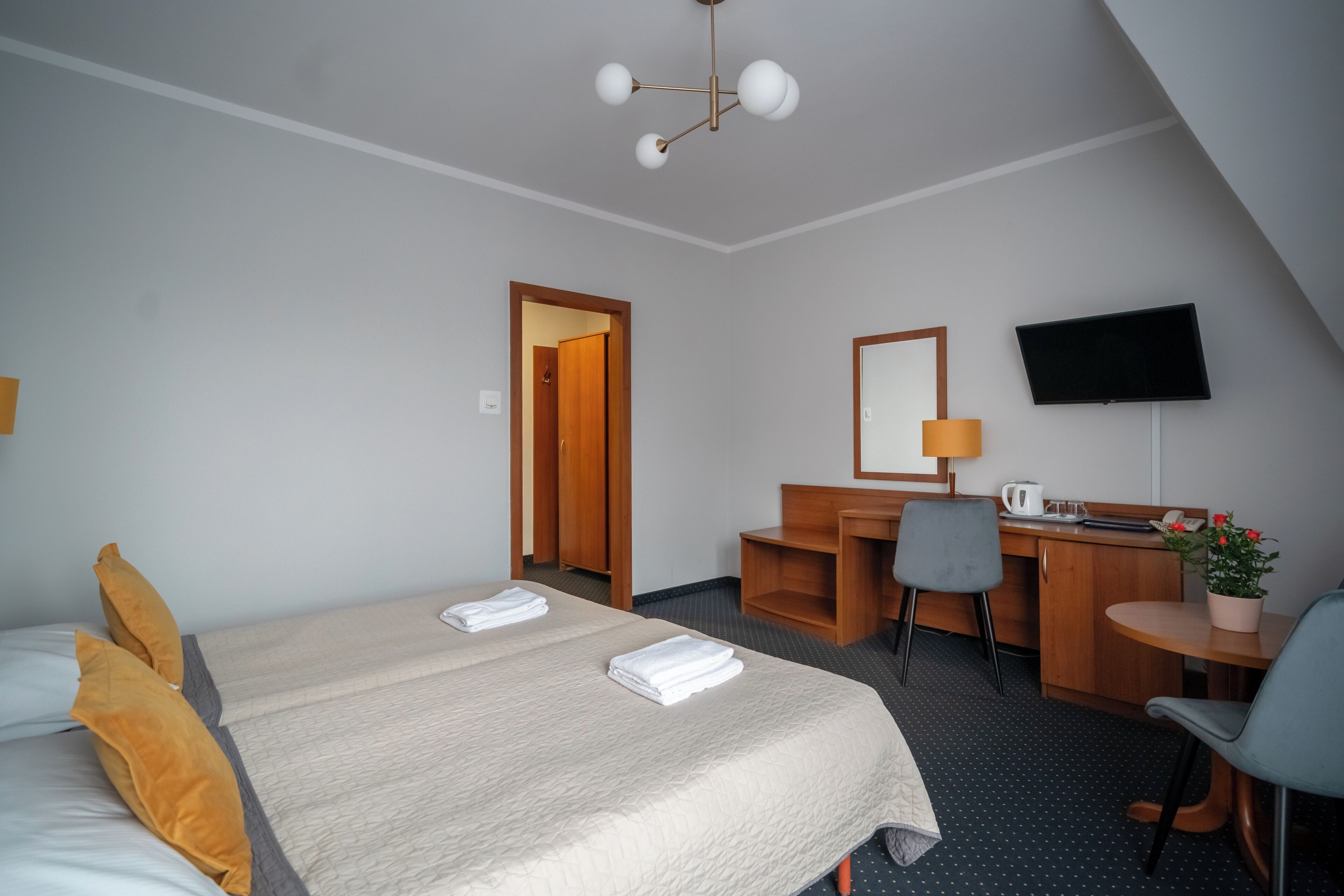 A hotel room with a bed, a desk, a chair, a television, and a small table with a plant.