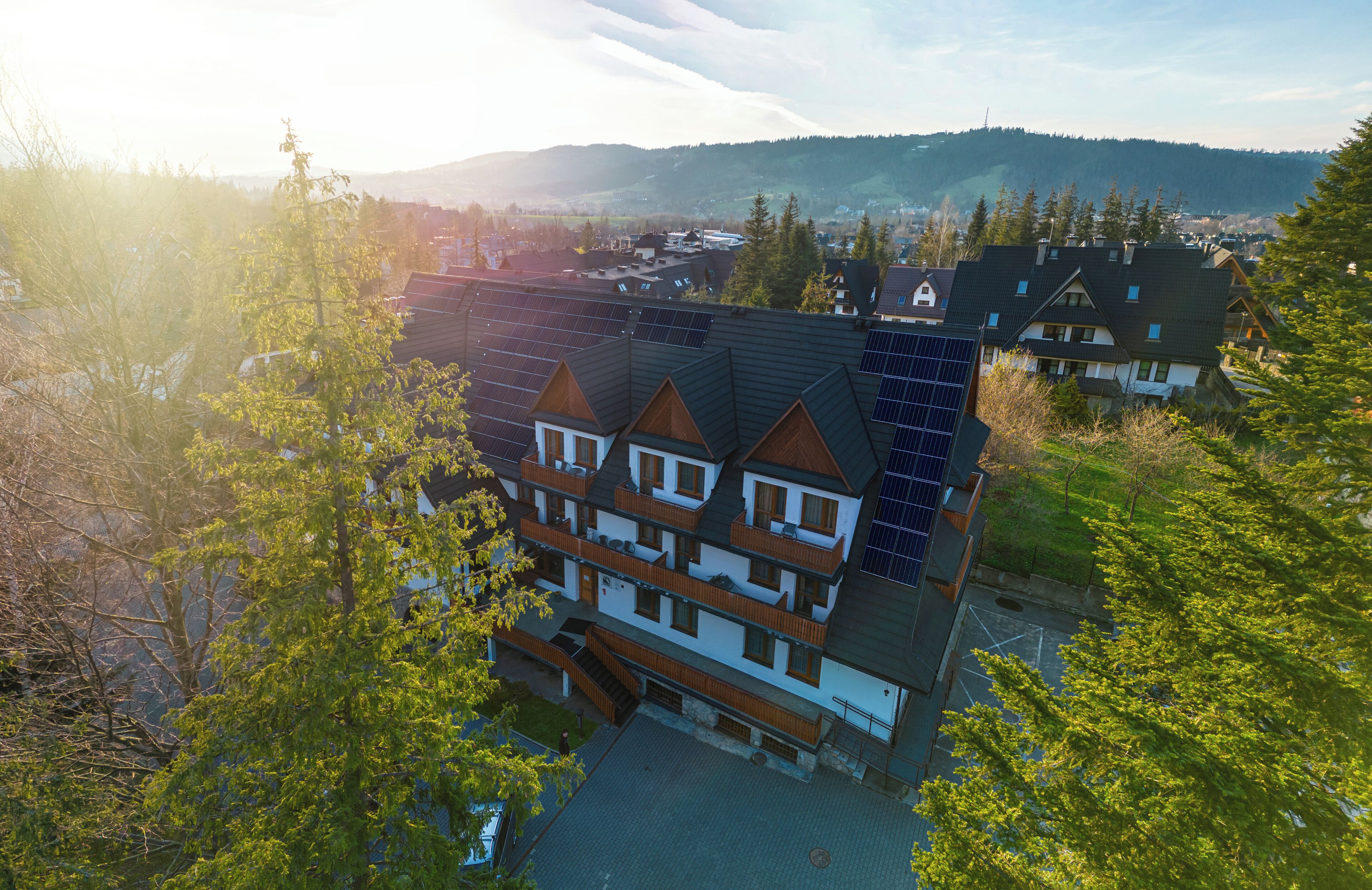 Un immeuble à plusieurs étages, doté de panneaux solaires sur le toit, entouré d’arbres et avec un paysage vallonné en arrière-plan.