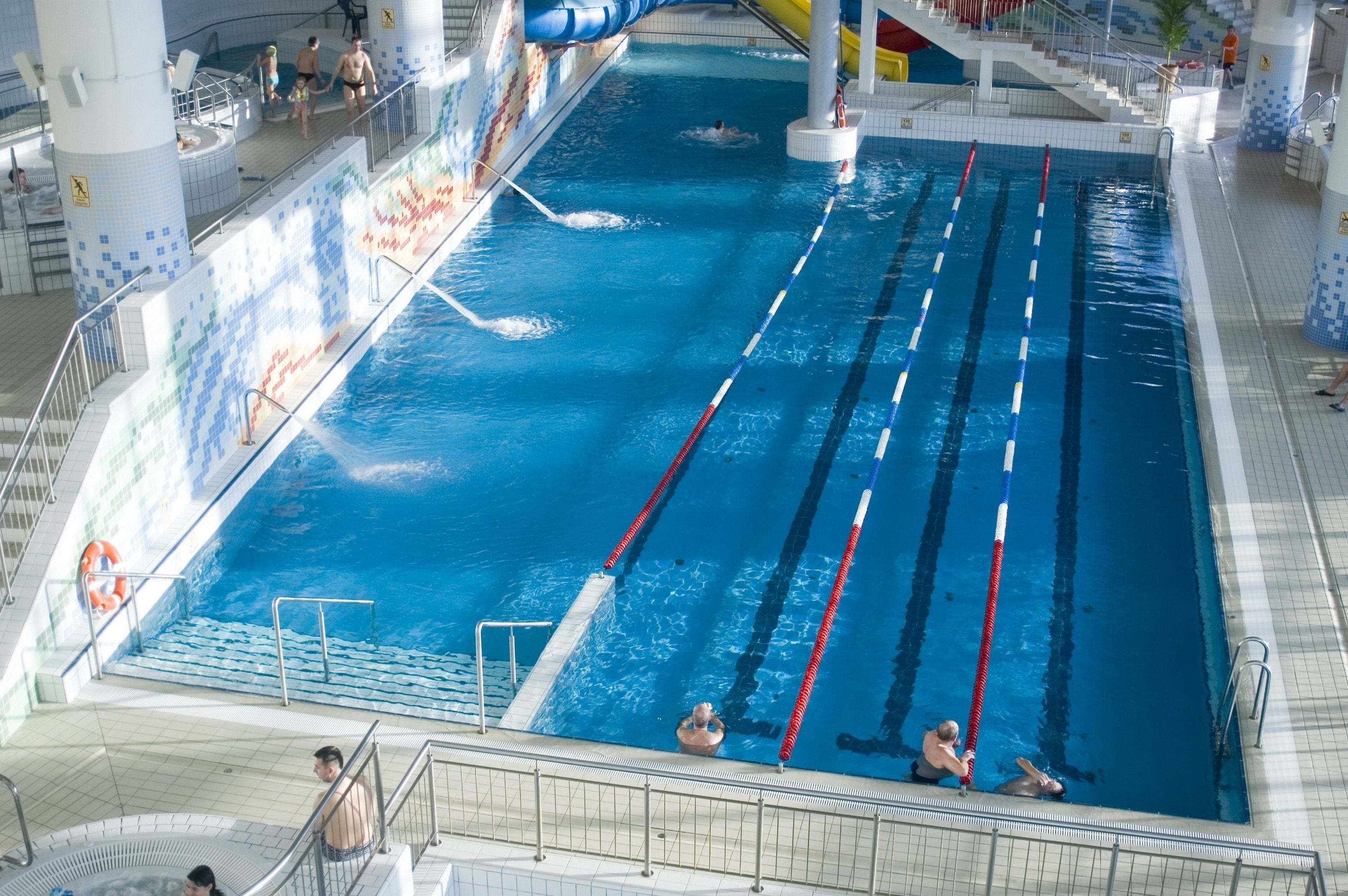 An indoor swimming pool with multiple lanes, a slide, and a hot tub area.