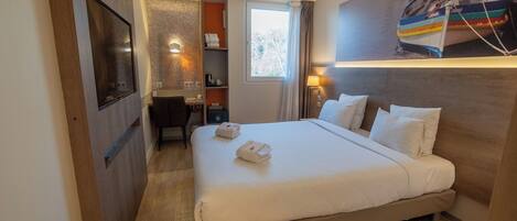 Habitación de hotel con una cama grande, un escritorio, una silla, un baño pequeño y una ventana.