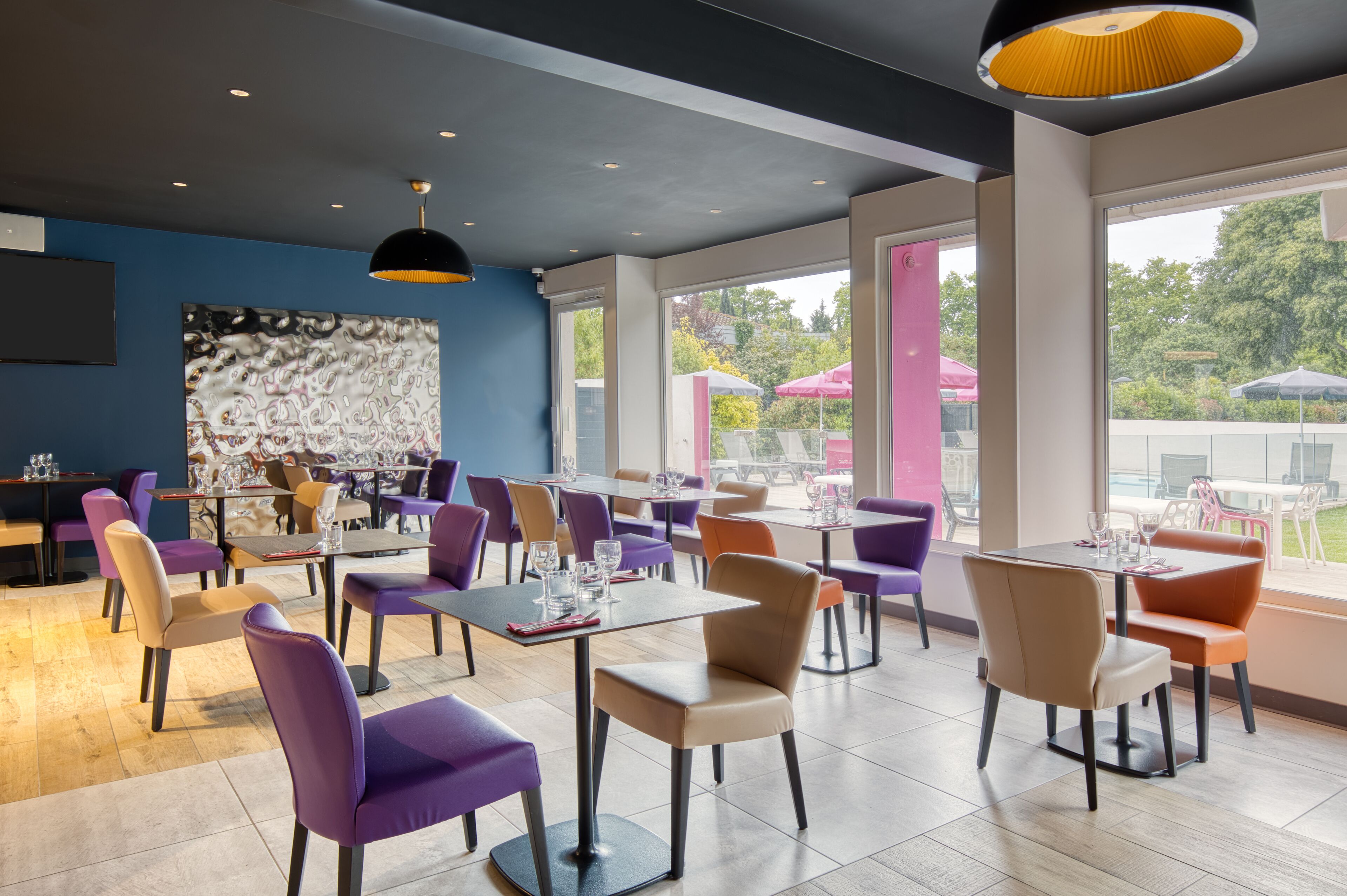 A modern restaurant with purple and beige chairs, large windows, and a black ceiling light.