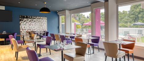 A modern restaurant with purple and beige chairs, large windows, and a black ceiling light.