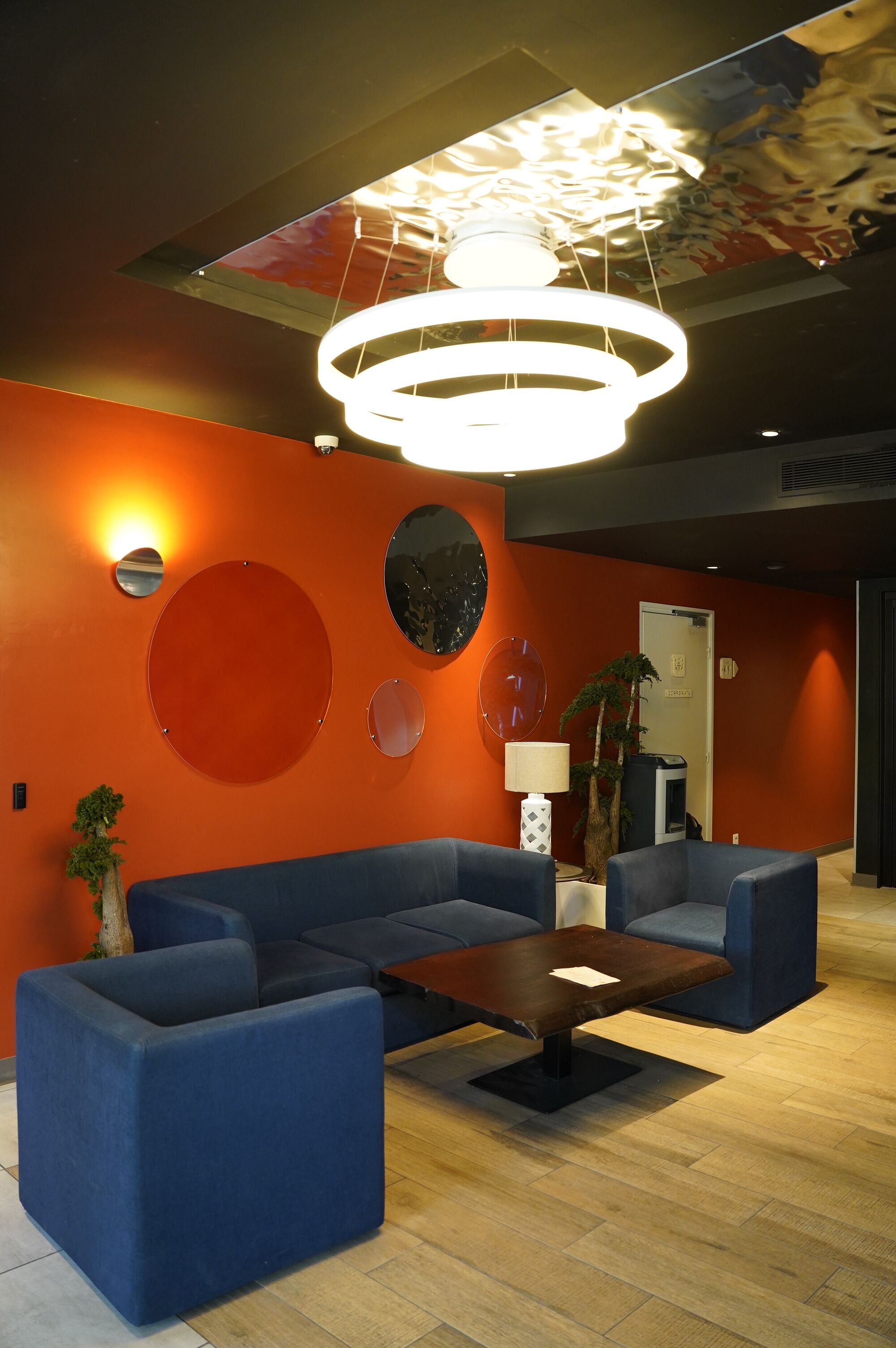 Een moderne lobby met een blauwe zithoek, een houten salontafel en een bijzondere ronde lamp.