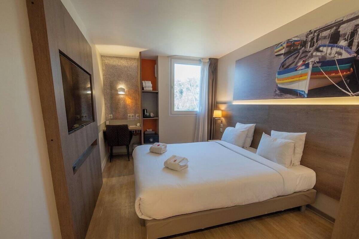 Habitación de hotel con una cama grande, un escritorio, una silla, un armario y un televisor montado en la pared.
