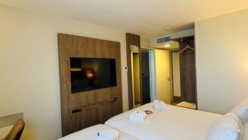 Habitación de hotel con dos camas, un televisor montado en un panel de madera, un armario y un espejo.