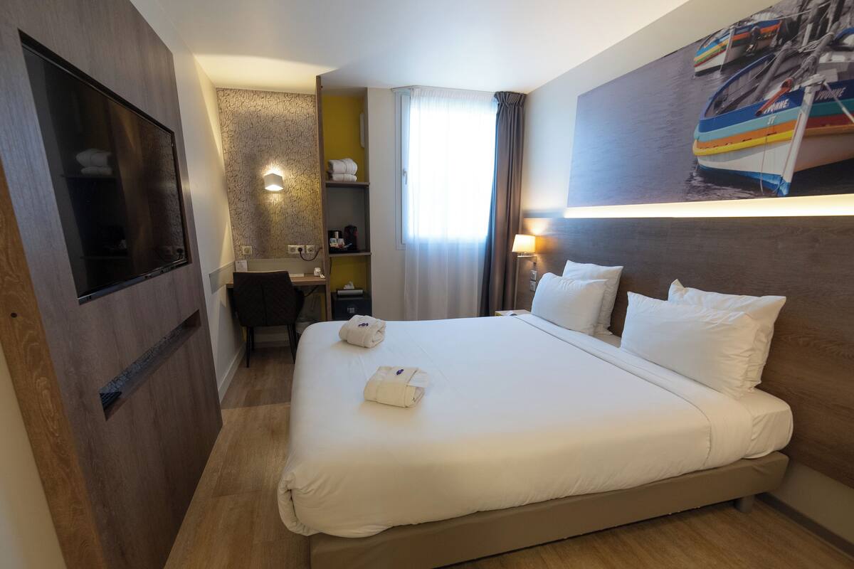 Habitación de hotel con una cama grande, un escritorio, una silla, un televisor, un baño pequeño y una ventana con cortinas.