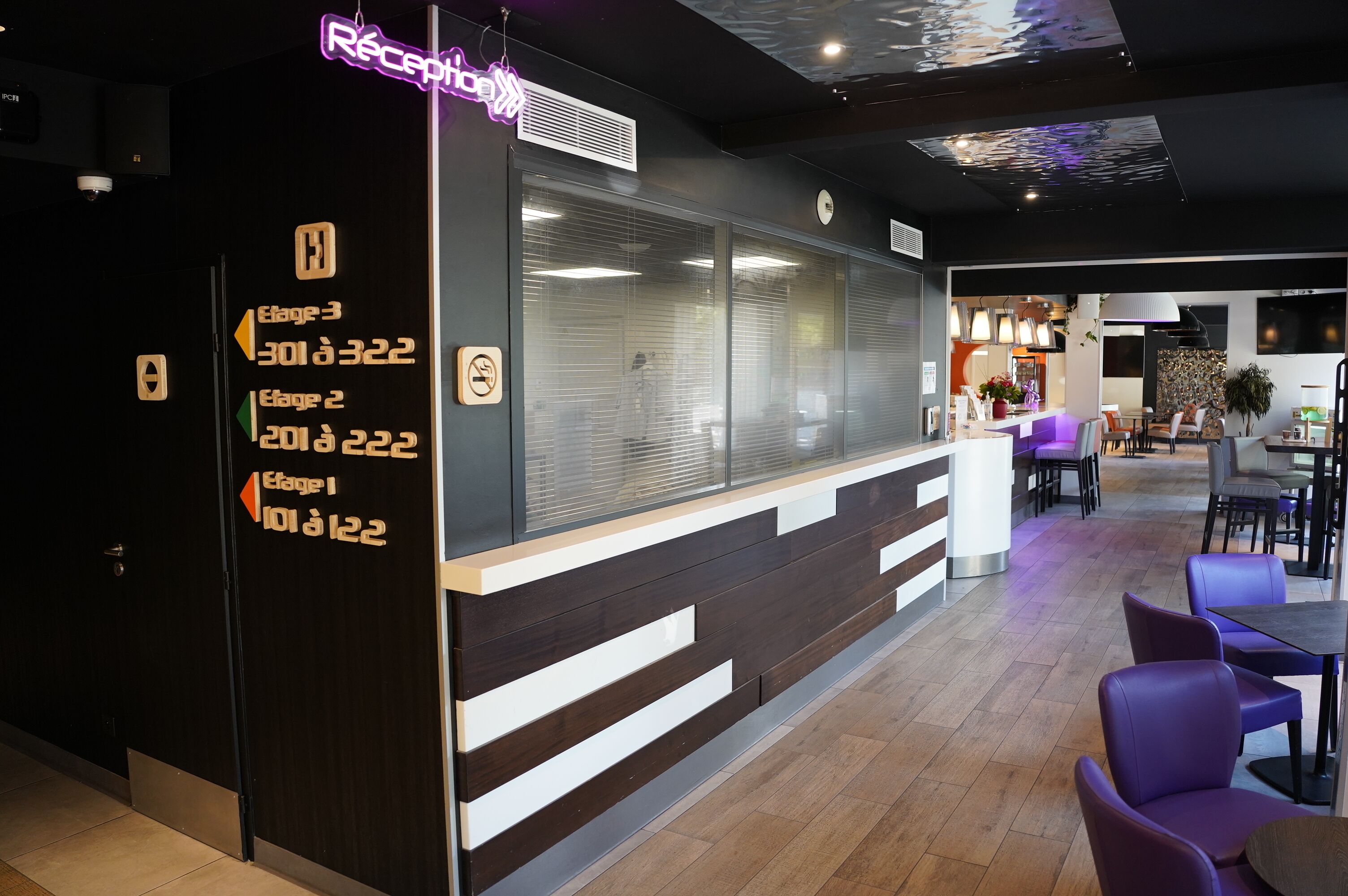Ett entréområde med en neonskylt, en receptionsdisk och skyltar som visar vägen till de olika våningarna i hotellet.