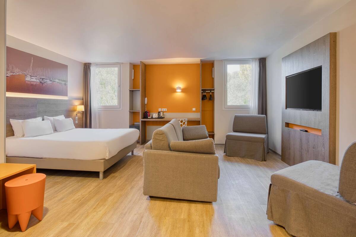 Una habitación de hotel con cama, sofá, sillón y televisión instalada en la pared.