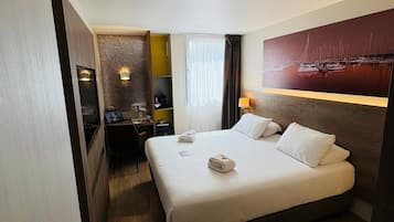Une chambre d’hôtel avec un grand lit, un bureau, une chaise, une petite table, une lampe et un tableau au mur.