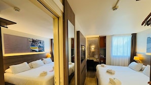 Habitación de hotel con dos camas, un escritorio, un espejo y vista a un barco a través de una ventana.