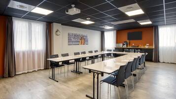 Une salle de conférence avec une longue table, des chaises, un projecteur et une horloge au mur.