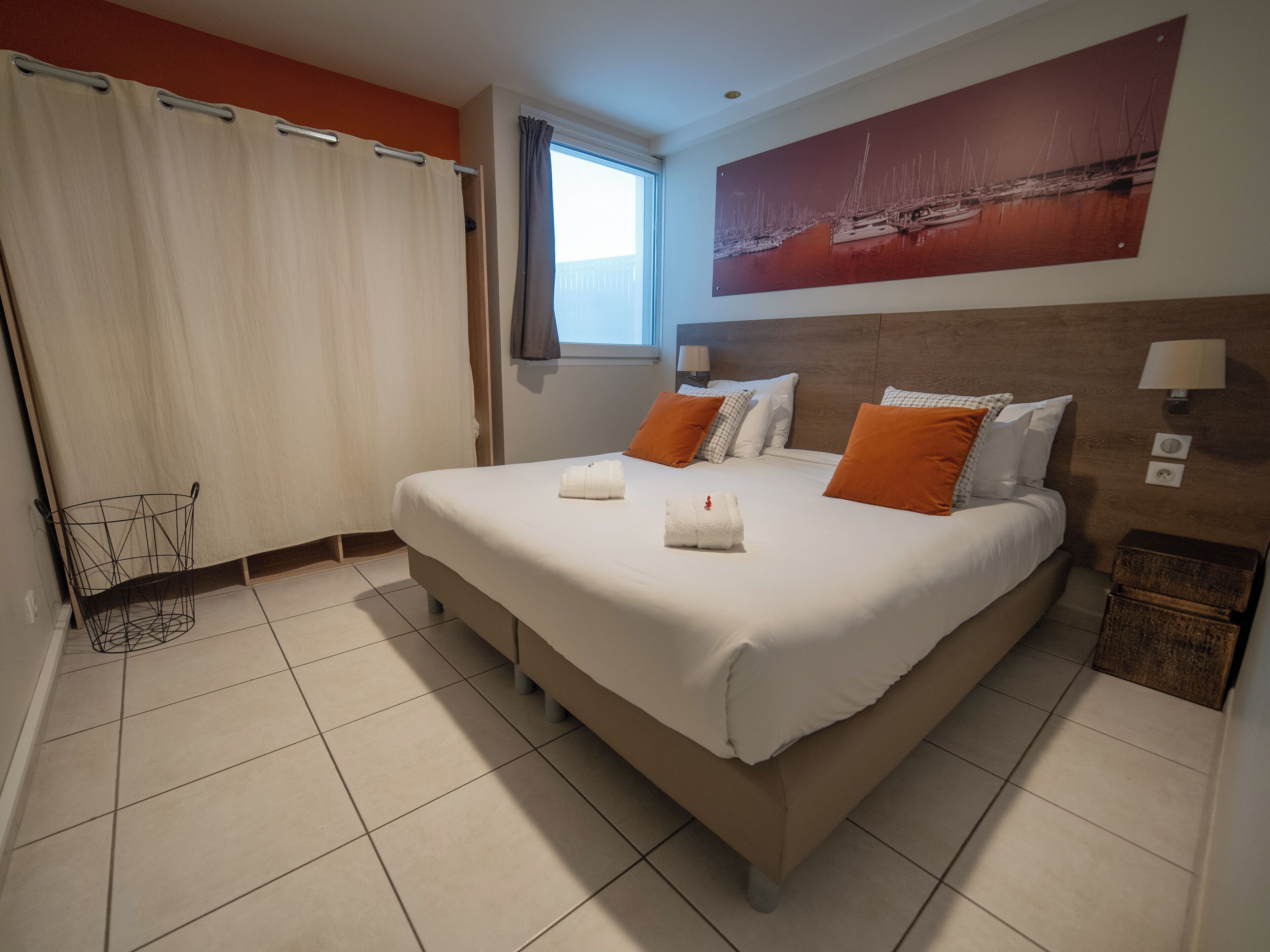 A hotel room with a large bed, two bedside lamps, a window with curtains, and a painting on the wall.