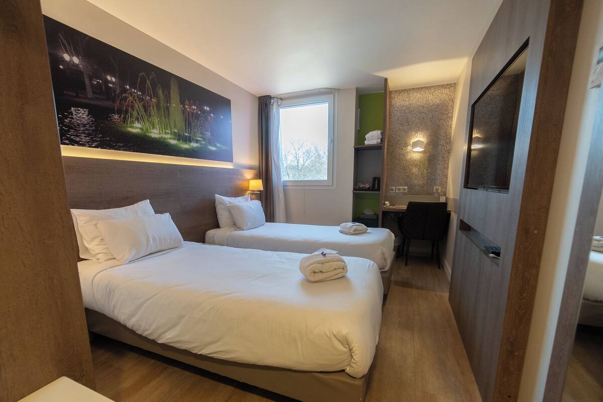 Habitación de hotel con dos camas, un escritorio, una silla, un televisor y un cuadro en la pared.