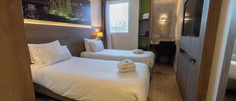 A hotel room with two beds, a desk, a chair, a TV, and a painting on the wall.