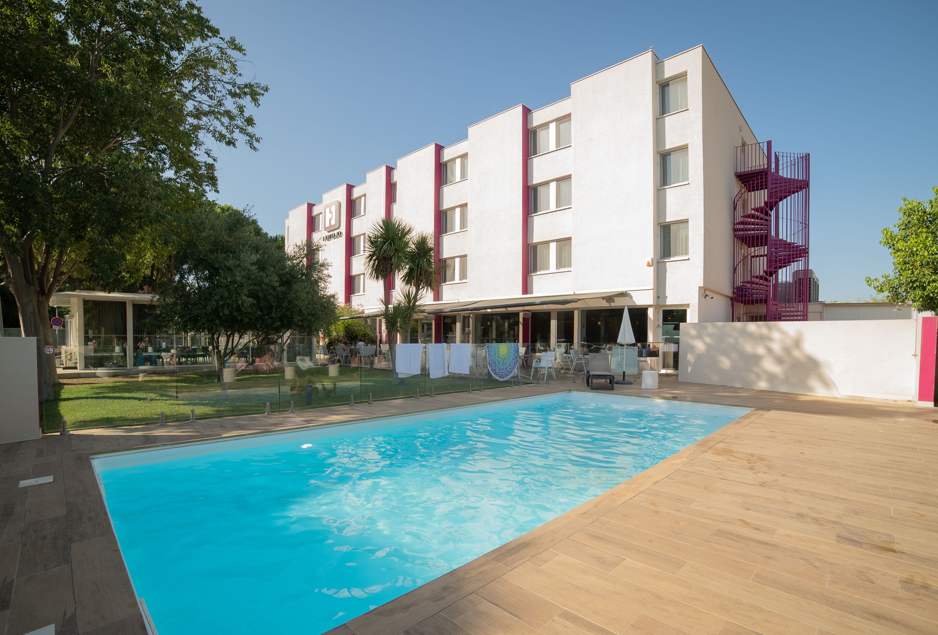 A hotel with a swimming pool, outdoor seating, and a modern building facade.
