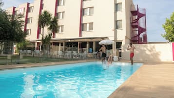 A hotel with a swimming pool, outdoor seating, and a modern building design.