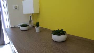 Een houten tafel met twee planten in potten en een witte lamp tegen een gele muur.