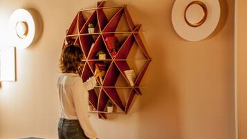 Une personne dispose des objets sur une bibliothèque dont les étagères présentent un motif géométrique, dans une pièce aux couleurs neutres et au décor moderne.
