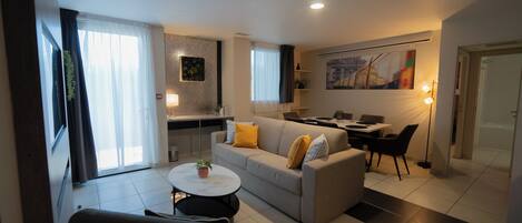 A modern living room with a sofa, a dining table, and a kitchen area.