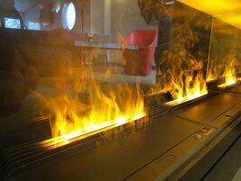 Una cocina con estufa a gas y una silla roja al fondo.