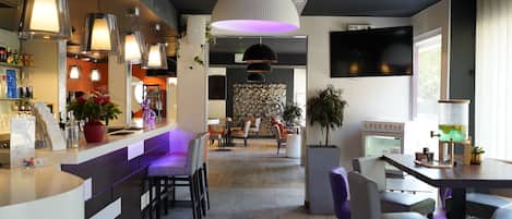 Zona de bar moderna con asientos, iluminación colgante y un televisor grande montado en la pared.
