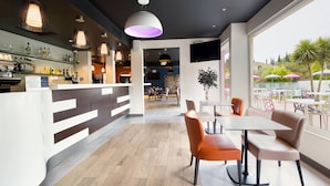 Eine moderne Bar mit einer Holztresen, Sitzgelegenheiten mit orangefarbenen und beigen Stühlen und Blick auf die Terrasse mit Sonnenschirmen.