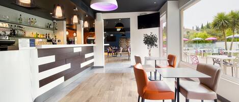 Eine moderne Bar mit einer Holztresen, Sitzgelegenheiten mit orangefarbenen und beigen Stühlen und Blick auf die Terrasse mit Sonnenschirmen.