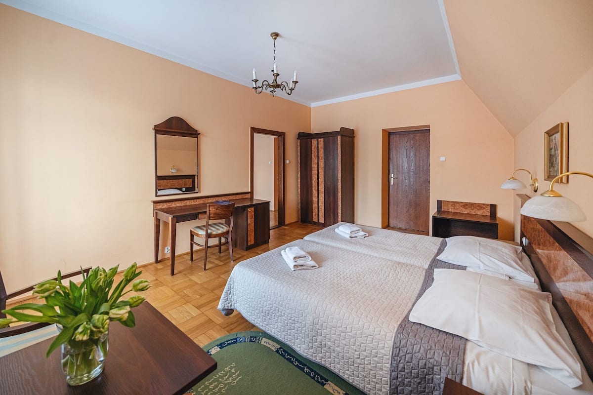 Une chambre d’hôtel avec un lit, un bureau, une chaise, un miroir et un lustre.