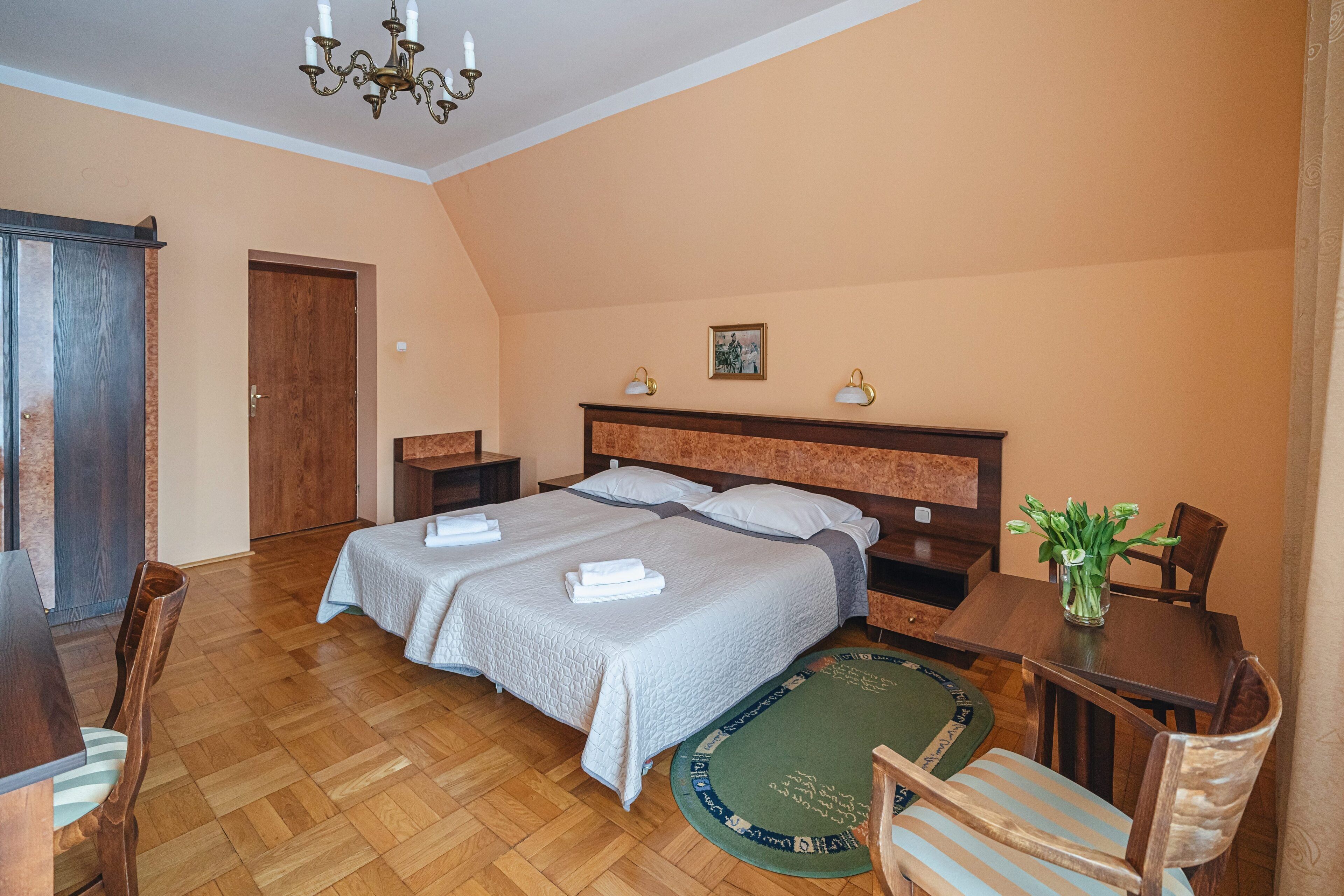 A hotel room with two beds, a wooden floor, a dining table, and a chandelier.
