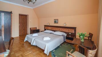 A hotel room with two beds, a wooden floor, a dining table, and a chandelier.