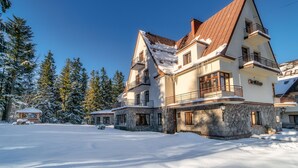 Ein großes, mehrstöckiges Gebäude mit einer Steinaußenfassade und mehreren Balkonen, umgeben von schneebedeckten Bäumen.