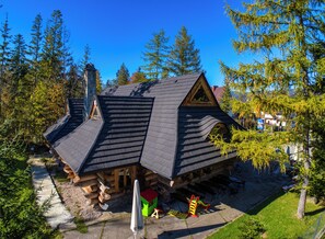 A log cabin with a steeply pitched roof, a chimney, and a small deck with outdoor furniture.