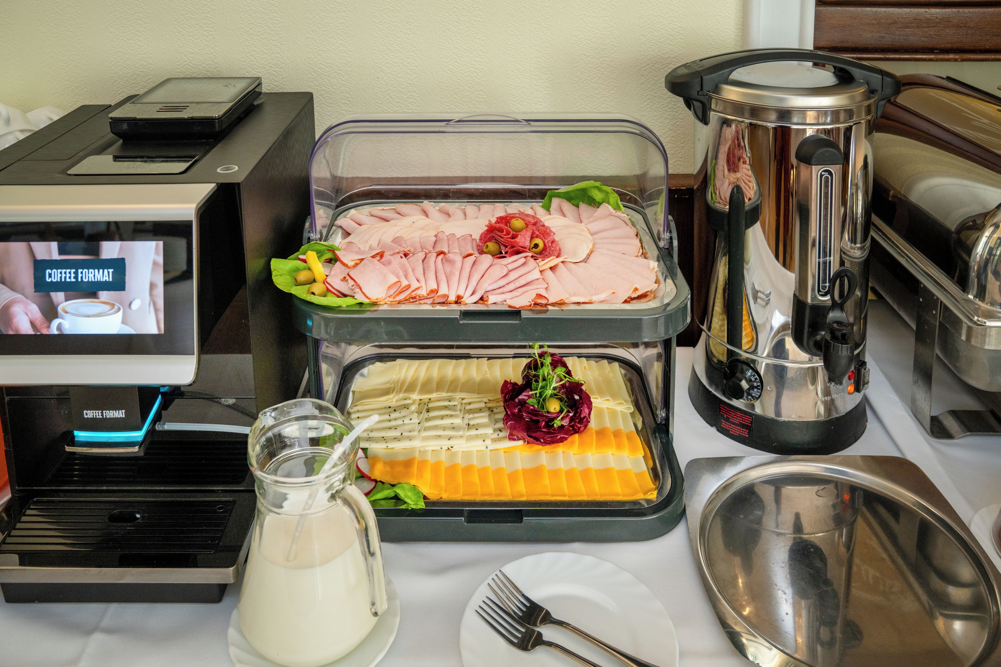 Una mesa de buffet con diferentes opciones de comida, una máquina de café y un dispensador de leche.