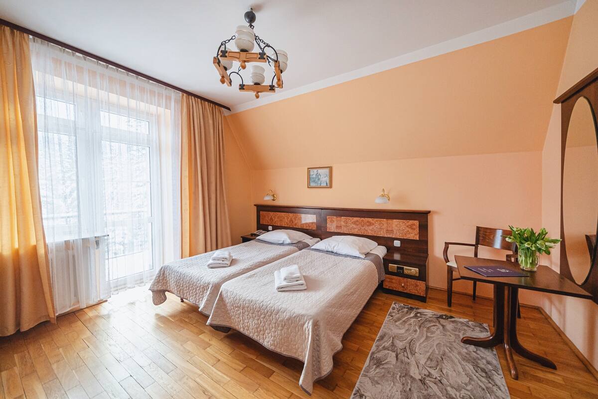 Une chambre d’hôtel avec deux lits, un plancher en bois, un lustre, une table à manger et une plante.