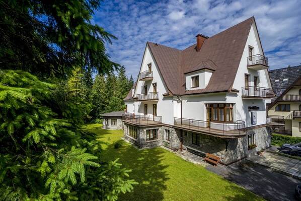 Ein zweigeschossiges Haus mit Steinunterbau, geneigtem Dach und einem Balkon.