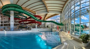 An indoor swimming pool with multiple water slides and a large glass window offering a view of the outside.