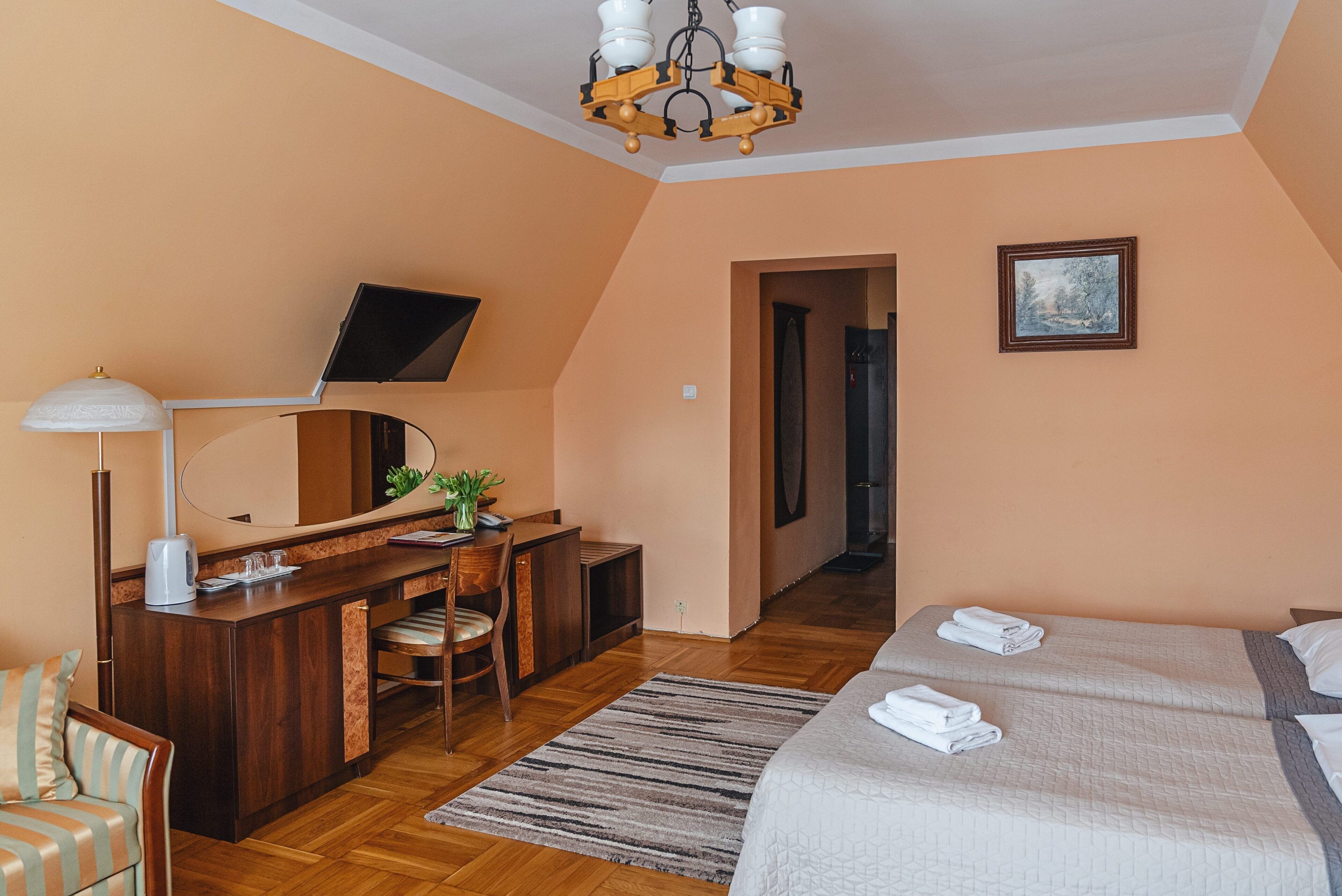 A bedroom with a bed, a desk with a chair, a mirror, a television, and a painting on the wall.