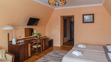 A bedroom with a bed, a desk with a chair, a mirror, a television, and a painting on the wall.