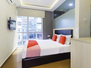 Une chambre d’hôtel dotée d’un grand lit, d’un téléviseur à écran plat fixé au mur et d’une fenêtre donnant sur les bâtiments environnants.