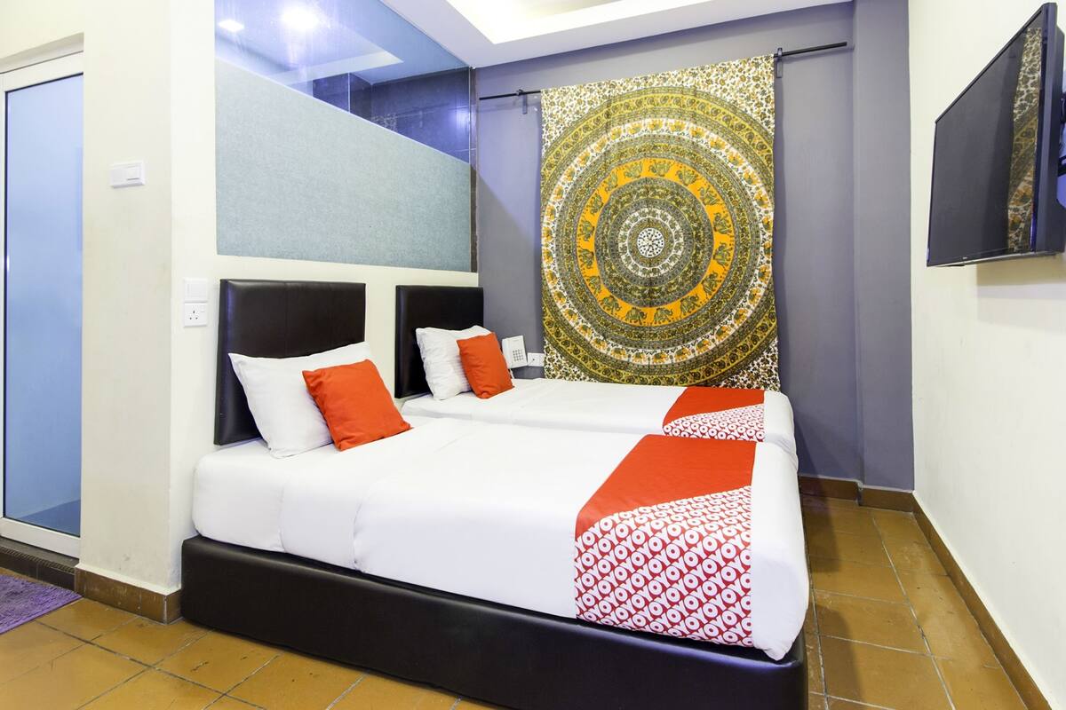 A double bed with white and red bedding, a tapestry, and a flat-screen TV on the wall.