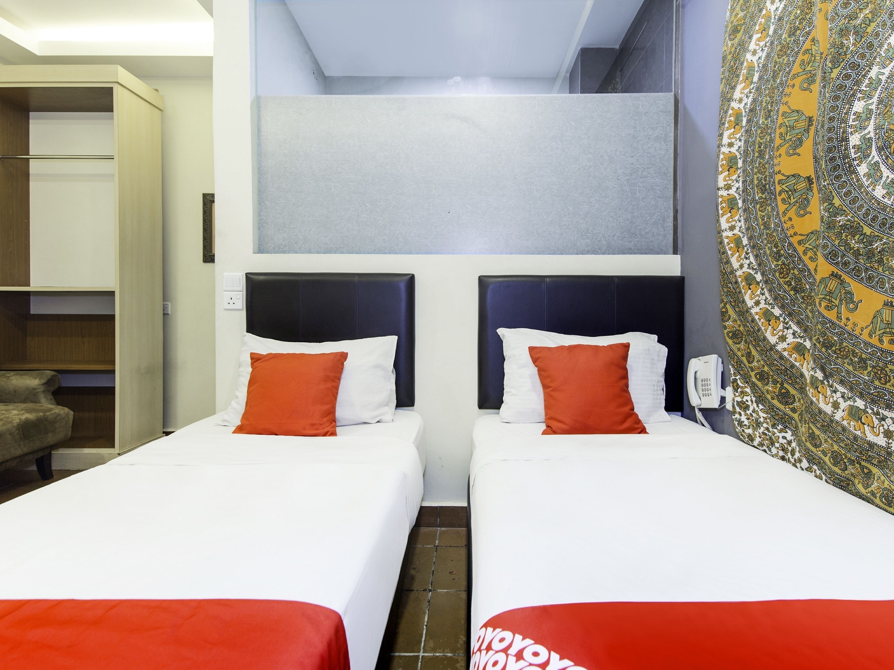 A hotel room with two single beds, a small seating area, and a patterned tapestry on the wall.
